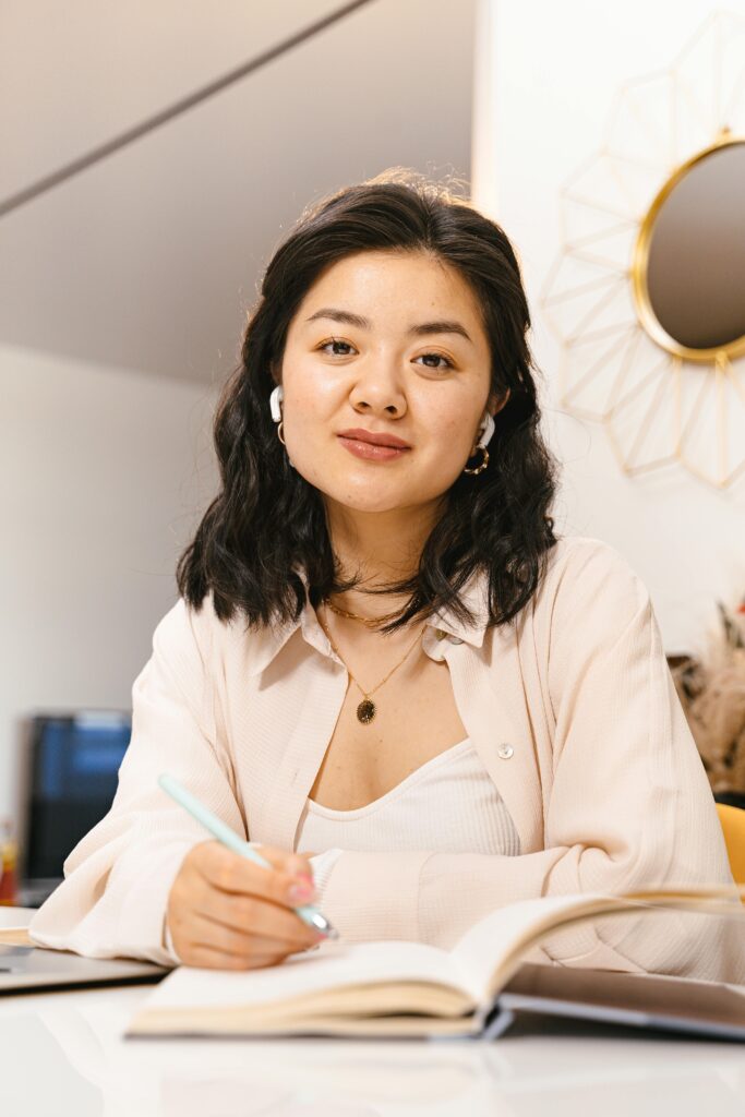 pexels-photo-8374294-8374294 Asian woman studying at home wearing wireless earbuds, holding a pen.